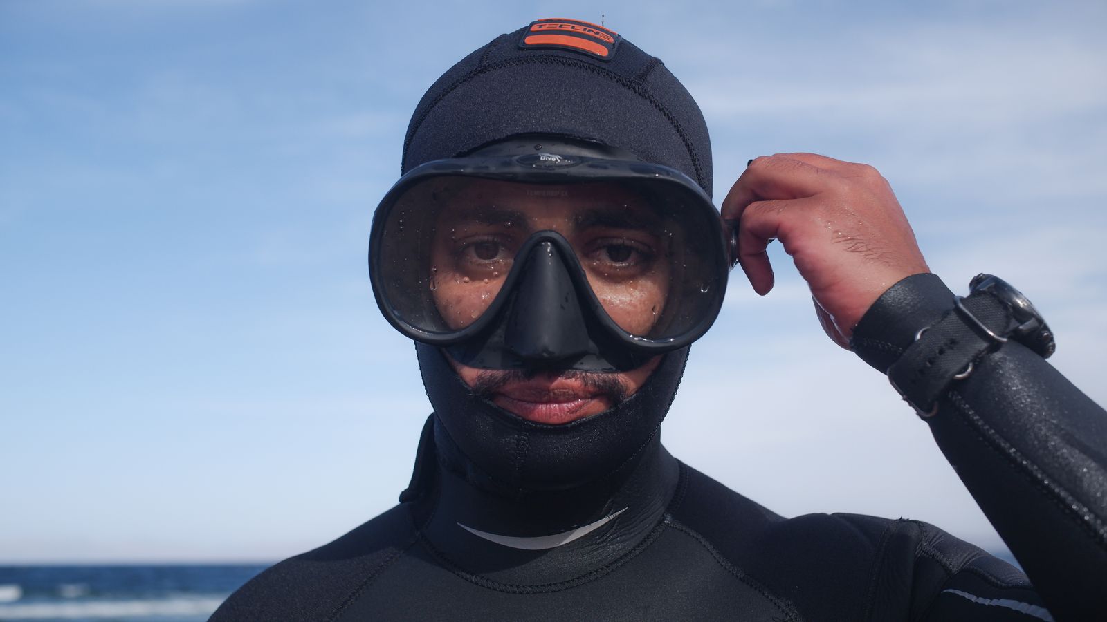 Diver adjusting a black diving mask before entering the ocean