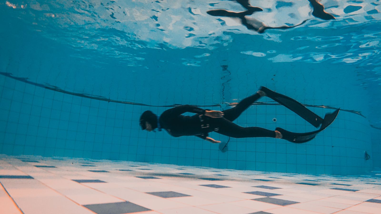 Freediver training underwater in a fitted black wetsuit